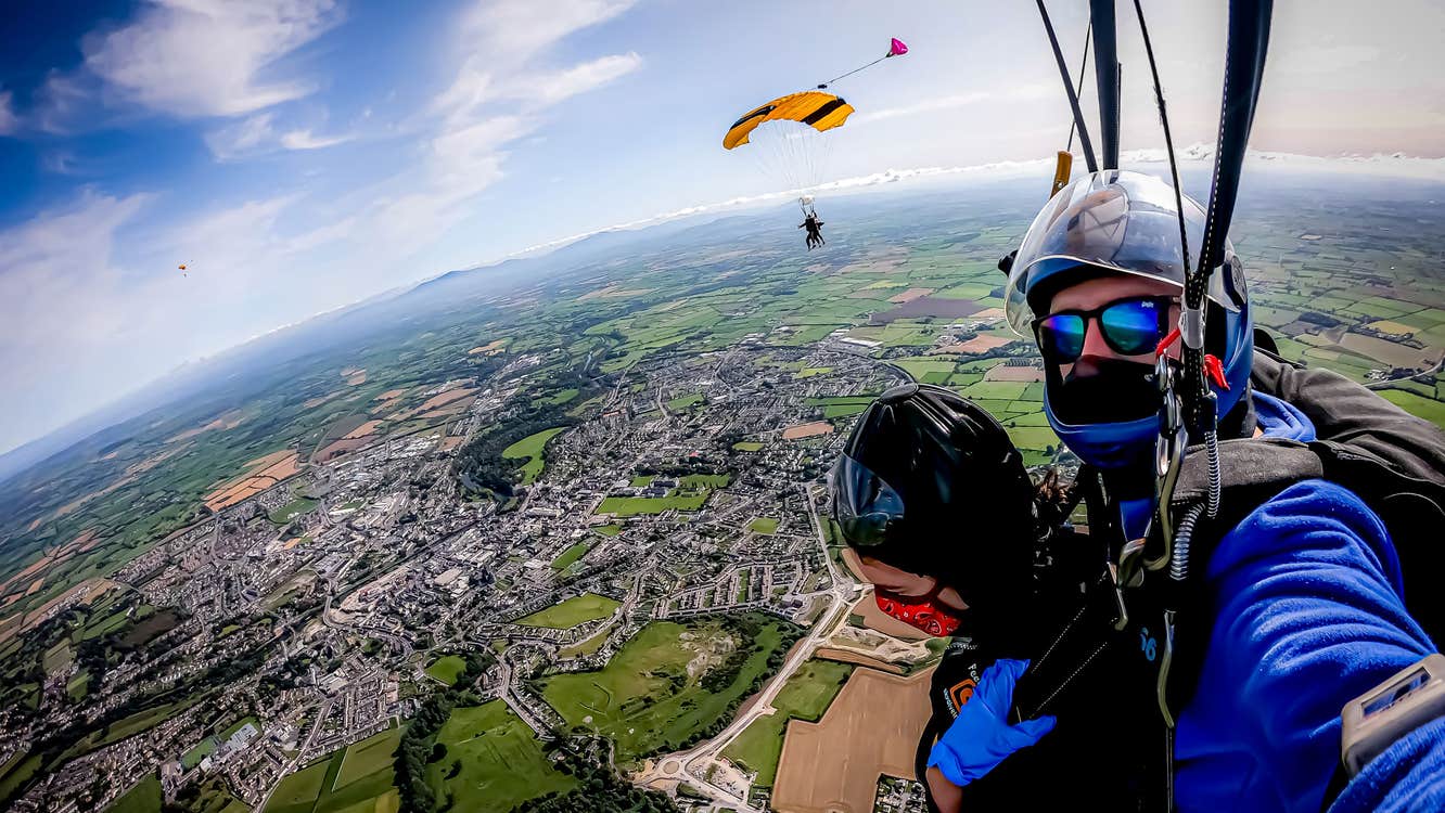 Tandem sky divers on way down with parachute open with views over kilkenny city below