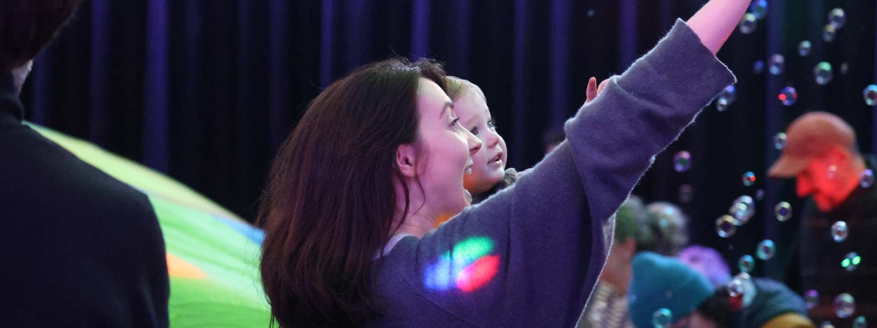 A laughing woman holding a baby pointing upwards with bubbles in the background.