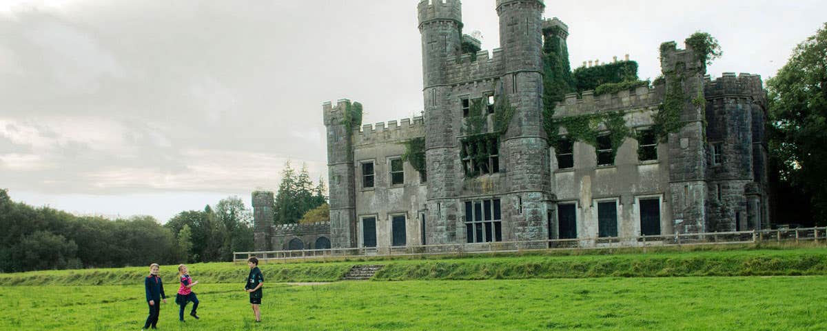 Image of three children on the lawn in front of the ruins of Castle Saunderson