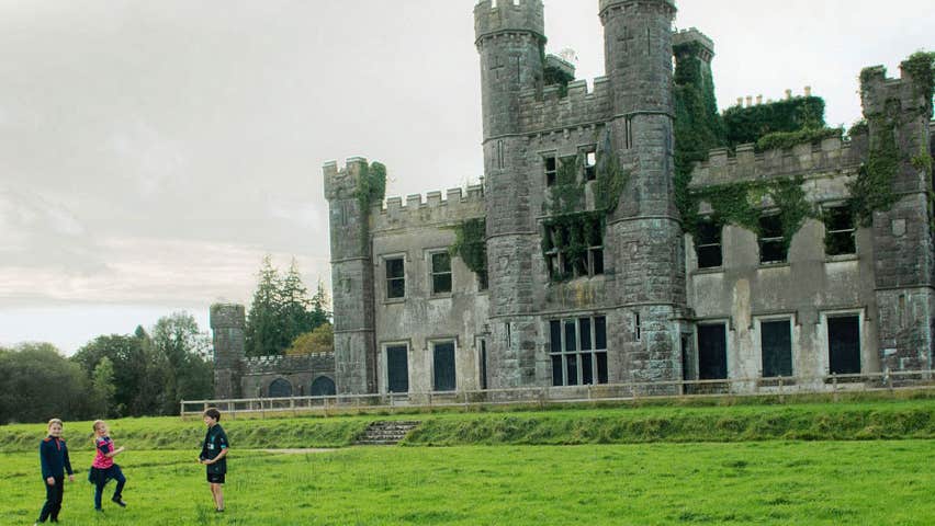 Image of three children on the lawn in front of the ruins of Castle Saunderson