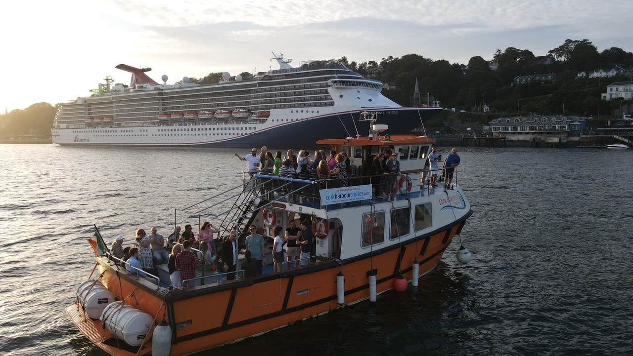 A boat with passengers in a harbour with a large cruise ship in the background