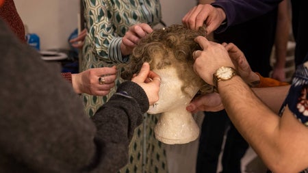 People looking at and touching a wig on a tour of a theatre