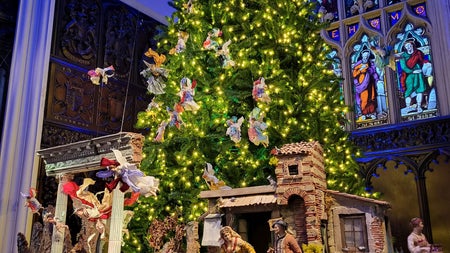 An elaborate, hand-crafted nativity scene sits beneath a glittering Christmas tree inside the Gothic Chapel Royal, its stained-glass windows glowing blue—a hidden gem showcasing Christmas tradition amid stunning ecclesiastical architecture.
