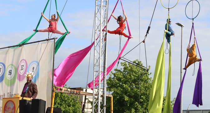 In the air, hanging from hoops attached to ropes, 4 performers with different coloured materials