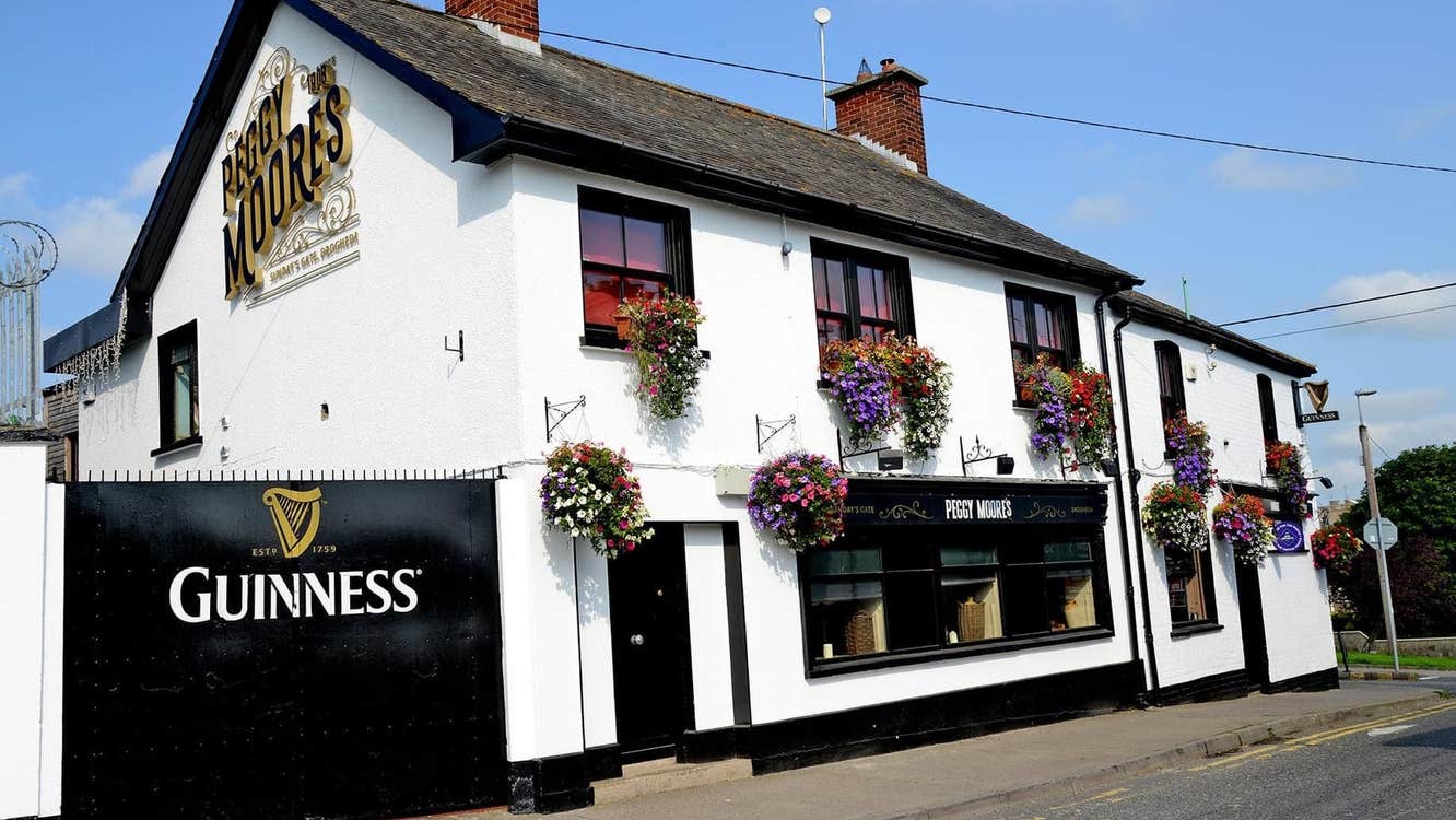 Exterior of a black and white pub on a street with flowers by the windows and in hanging baskets