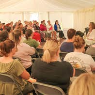 An audience in a large tent listening to a person at the front talking.