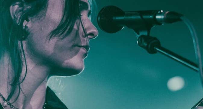 Close up side view of woman in front of a mic on a stand, playing a guitar.