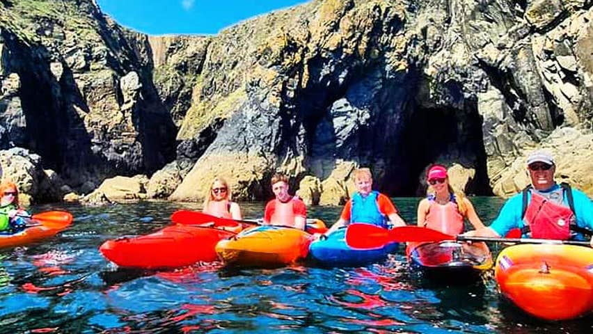 A group of six sea kayakers posing in front of caves at Newtown Cove