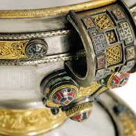 Close up shot of part of ancient, ornate bowl decorated with silver and gold motifs.