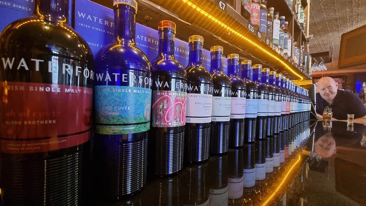 A row of wine bottles with the bartender at the far end looking towards the camera