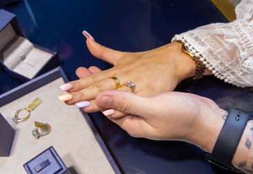 A close up of rings on fingers with a selection of rings on a counter