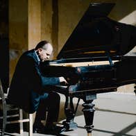 A man is seated playing a grand piano