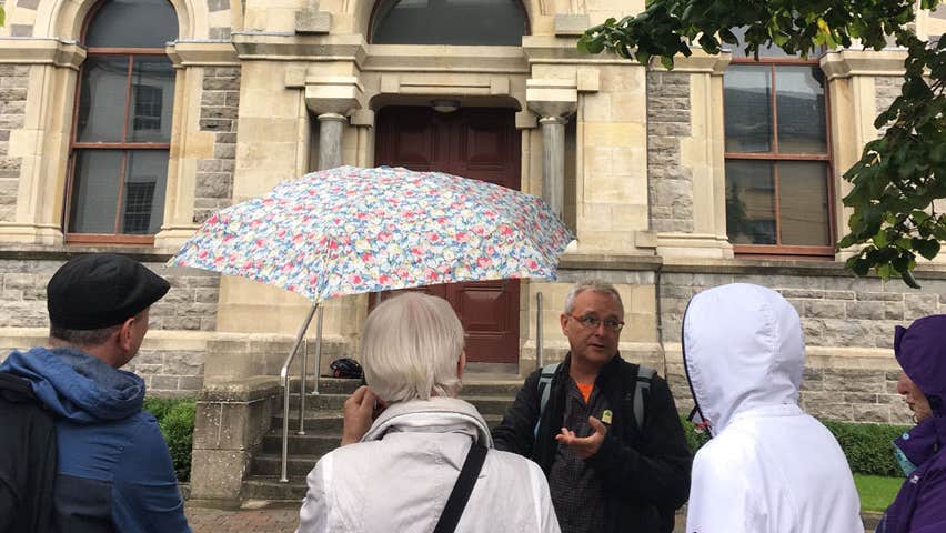 A group of people standing outside an old building while a tour guide speaks to them