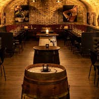A stone walled room with a vaulted ceiling with wooden tables and beer barrels