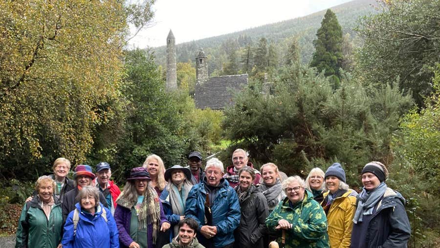 A group on a Glendalough Musical Tour with the round tower and Saint Kevins church in the background