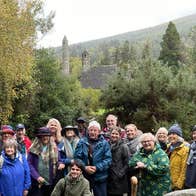 A group on a Glendalough Musical Tour with the round tower and Saint Kevins church in the background