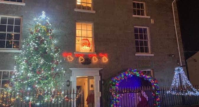 The front view of large, Georgian style building lit up at christmas with large tree.