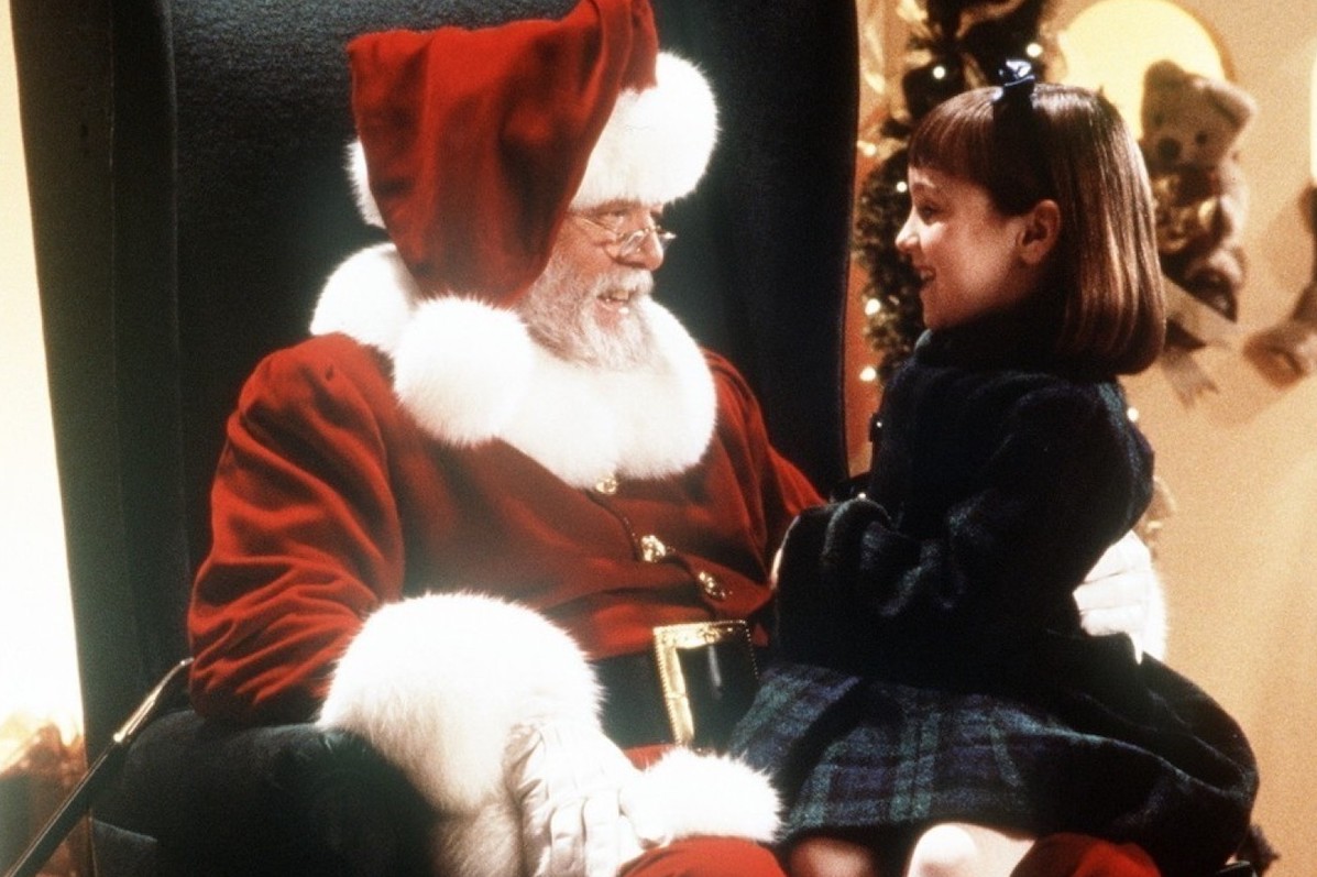 A santa is talking to a young girl who is smiling.