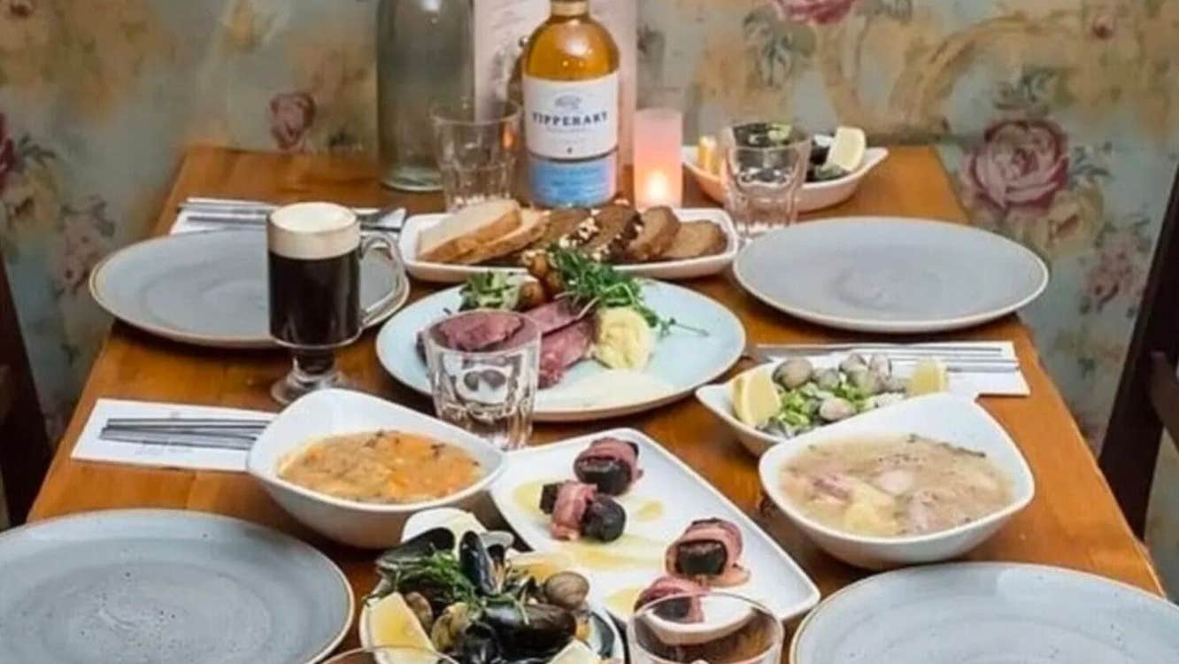 Table with four grey plates an assortment of food dishes glasses a bottle of wine and a candle