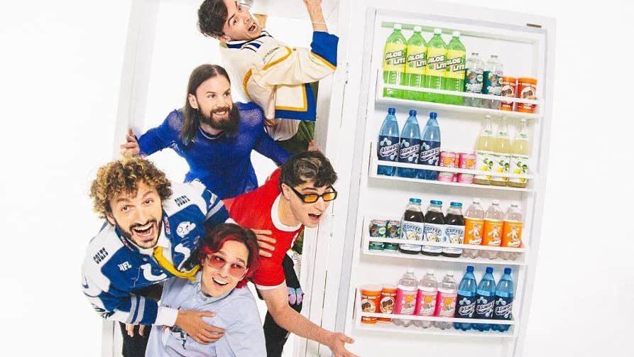 5 men bursting out of a large fridge full of bottles in the door