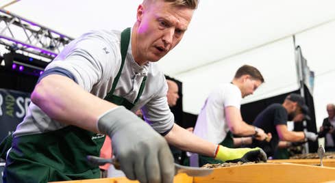 Anti Lepick, 2022 champion, in action. A close up shot of a man in an apron wearing gloves with a wooden tray in front of him with oyster in a white marquee.