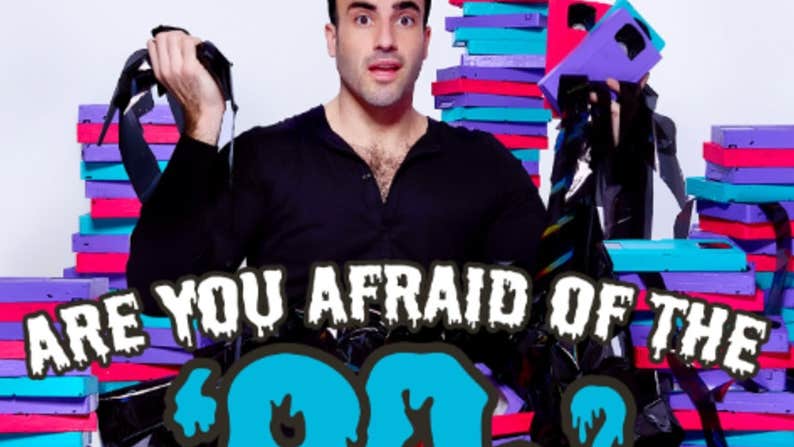 Rob Anderson: Are You Afraid of the 90s? A questioning man holding tape from old video cassettes with piles of tape boxes behind him in 3 different colours.