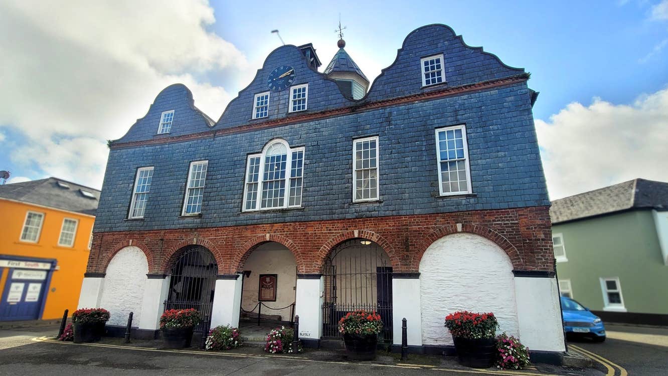 Slate red brick and white exterior of a dutch style building with three open archways and flowers outside