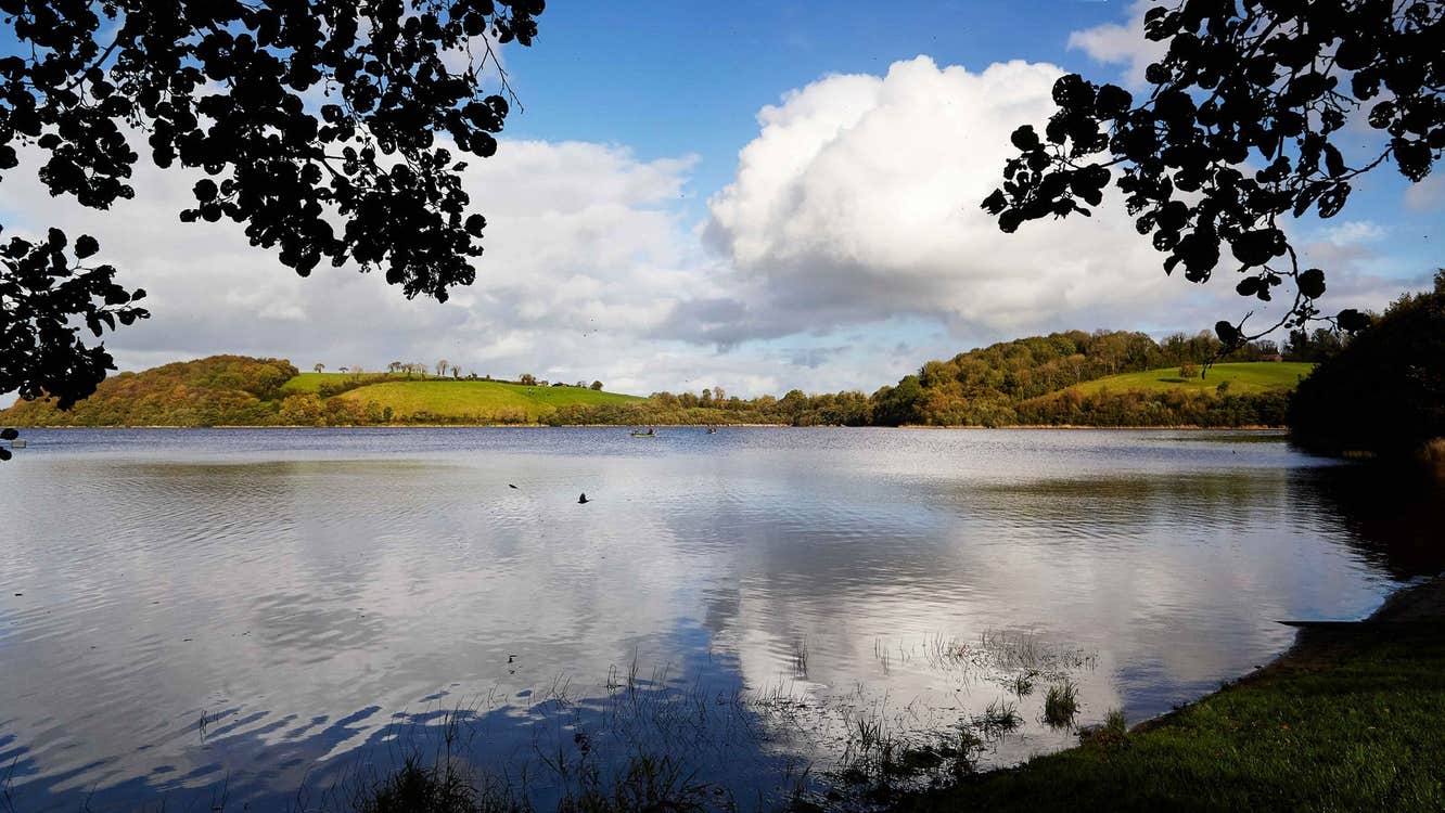 A view of a lake with some ripples and a cloud reflected on it