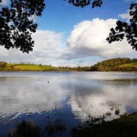 A view of a lake with some ripples and a cloud reflected on it