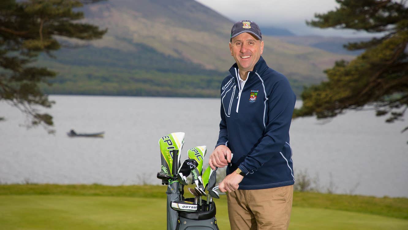 Mark Heinemann of Getgolfing.ie with a set of golf clubs on a golf course standing in front of a lake