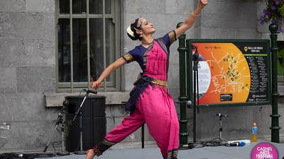 A woman dressed in dark pink and black Indian style outfit is dancing on a small stage