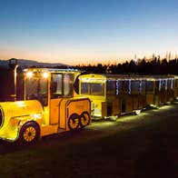 A small yellow train with carriages lit up at dusk
