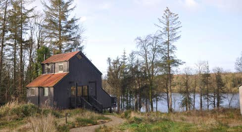 A brown cabin surrounded by trees sitting beside a lake.