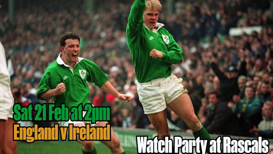 2 men playing rugby in green shirts with large crowd in background.