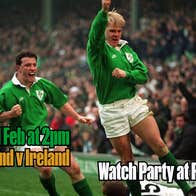 2 men playing rugby in green shirts with large crowd in background.