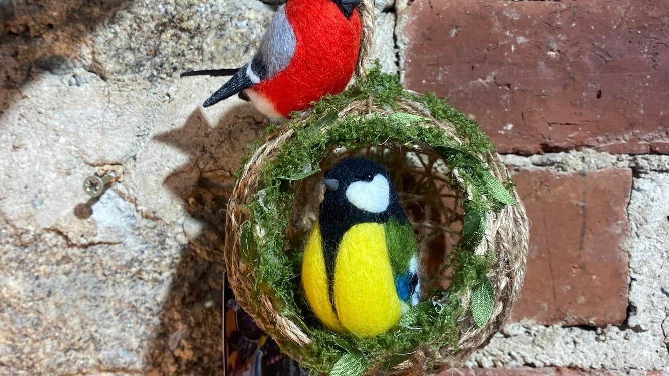 A felt brightly coloured bird in a small round woven half open ball with another felt brightly coloured bird on the top.