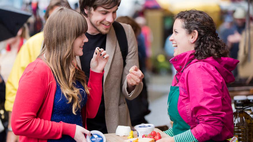 A merchant offering two people samples at the Galway Farmers' Market.