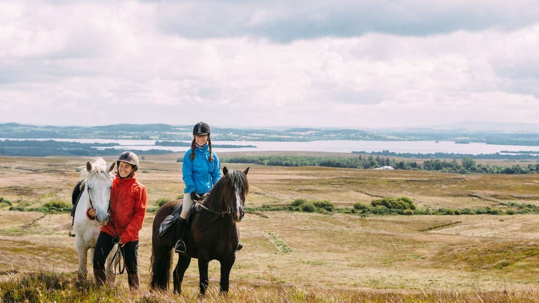 A child and an adult on a horse riding expedition with beautiful sea and mountain views