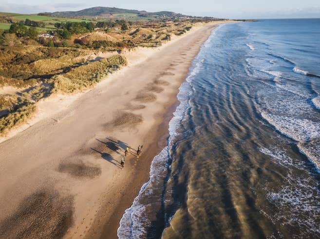 Aerial shot of three people horse riding on Brittas Bay beach in County Wicklow.