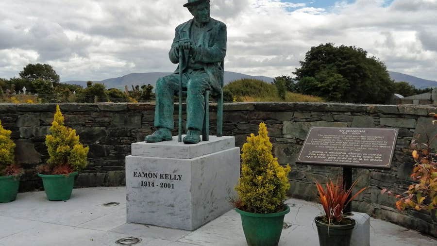 Bronze life sized seated statue of Eamon Kelly in a storytelling pose on a marble plinth