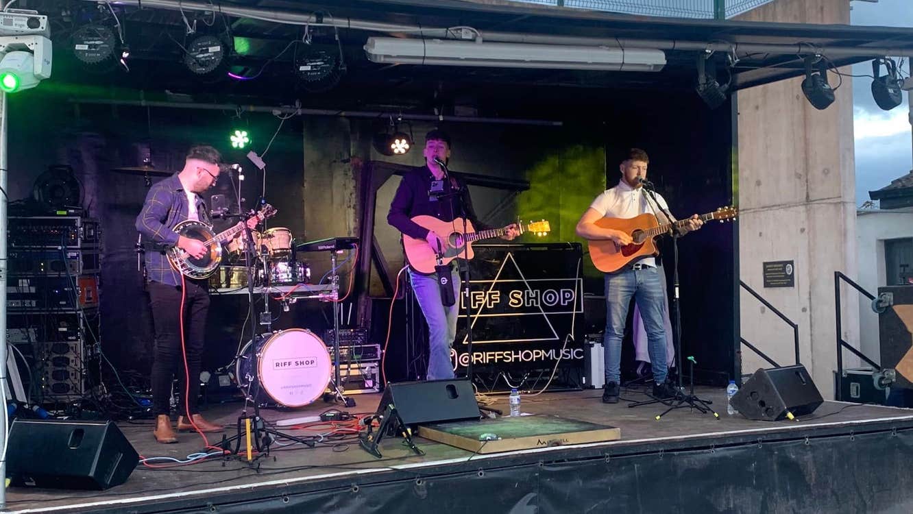 3 men playing guitar in a band on a small stage outdoors.