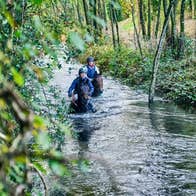 Two jockeys riding their horses down a river