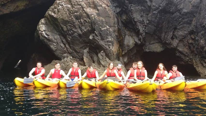 A group of young kayakers lined up by an entrance to a sea cave on Arranmore Island