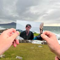 Two hands holding up a picture of a scene from the film, Banshees of Inisherin, that was filmed in that location. The scene pictures actor Colin Farrell expressing a sad face.