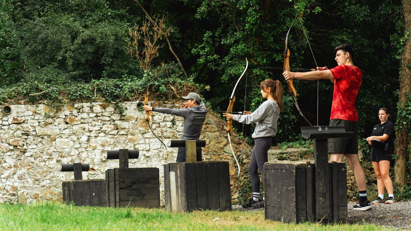 Three people practice archery with an instructor standing behind them