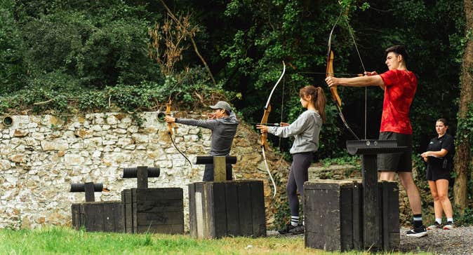 Three people practice archery with an instructor standing behind them