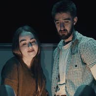 A woman and slightly anxious looking man looking down at something obscured from the viewer, dimly lit.