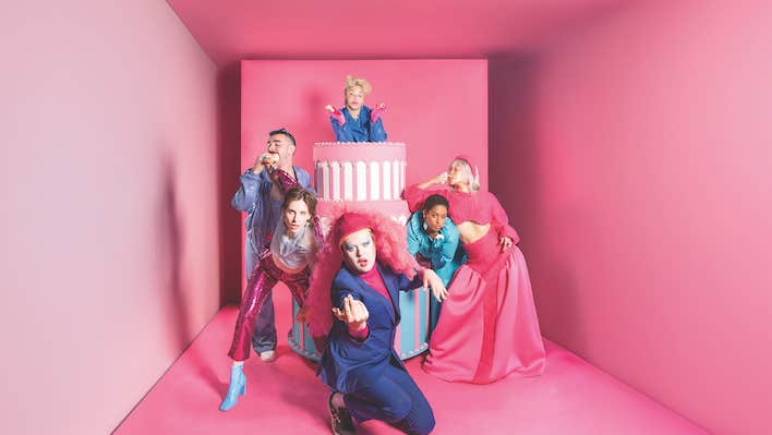 A small, narrowing pink room with people in various poses dressed in shades of pink and blue.