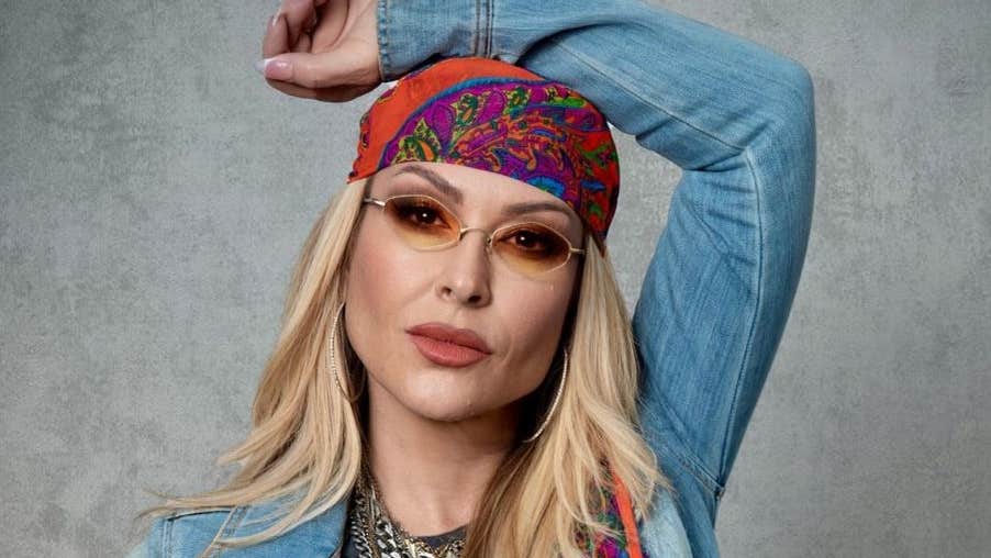 Pop icon Anastacia, a woman wearing small sunglasses and a headscarf with her left arm resting on the top of her head.
