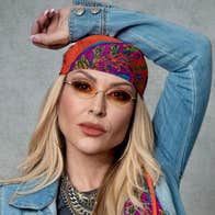 Pop icon Anastacia, a woman wearing small sunglasses and a headscarf with her left arm resting on the top of her head.